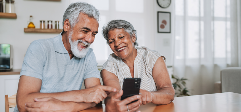 Smiling senior couple sitting at their kitchen table looking at a smartphone together